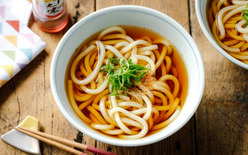 Japanese bowls containing Classic Udon Noodle Soup called Kake Udon or Su Udon, topped with sliced green onion and shichimi togarashi (Japanese seven spice).