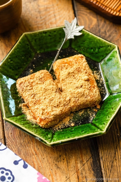 A green plate containing Japanese rice cake (mochi) coated with kinako (soybean flour).