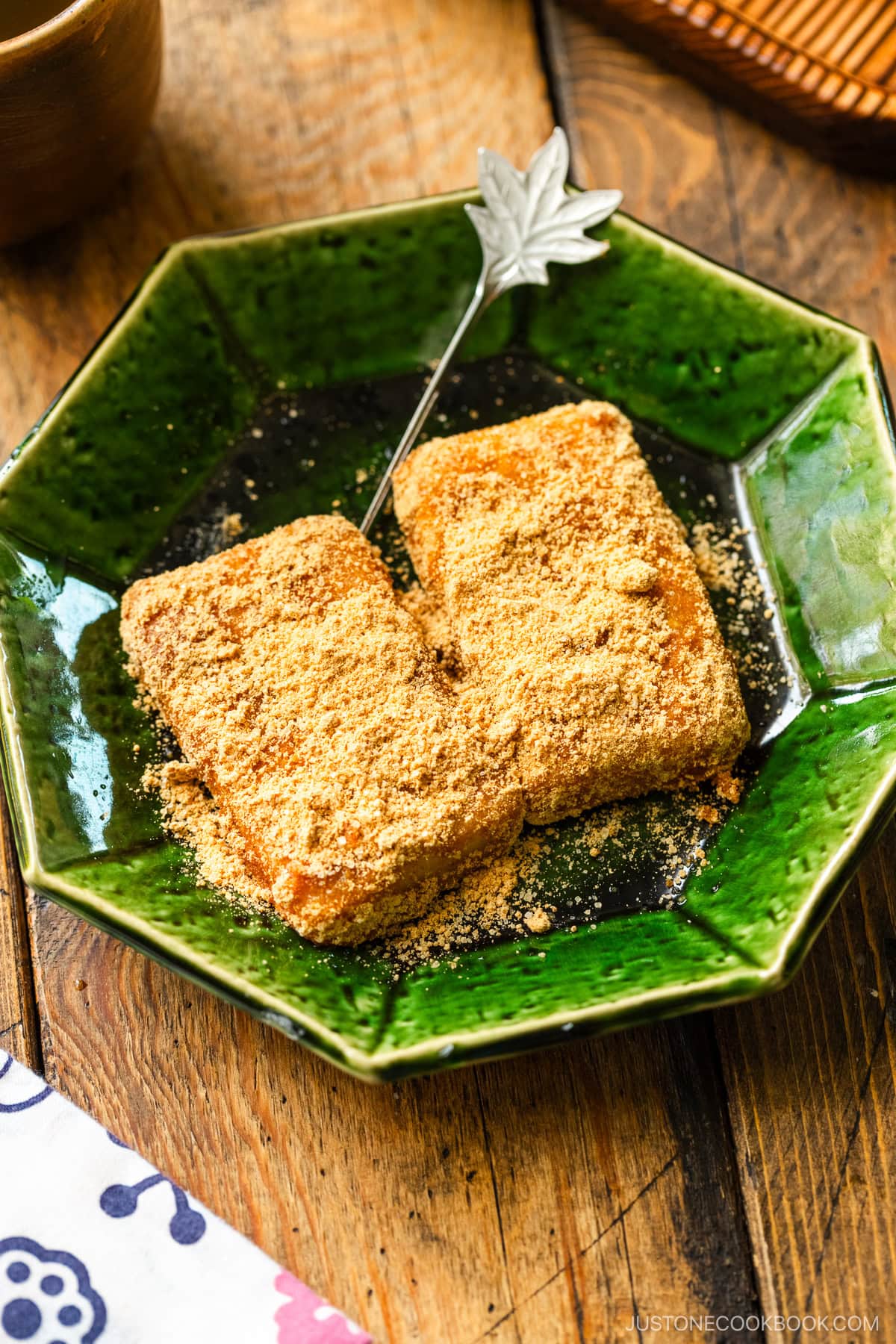 A green plate containing Japanese rice cake (mochi) coated with kinako (soybean flour).